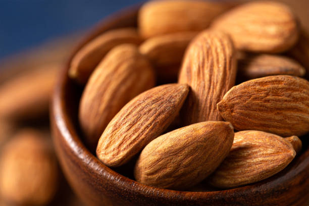 Extreme close up of fresh raw almonds in a brown wooden bowl