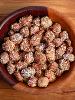 Sweet peanuts with coconut in a wooden bowl on a cutting board.