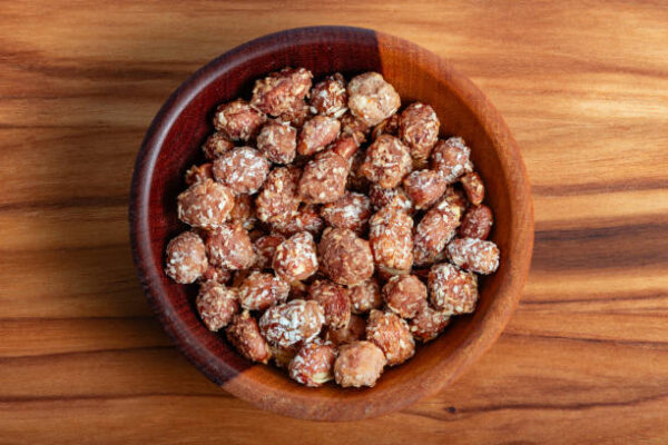 Sweet peanuts with coconut in a wooden bowl on a cutting board.